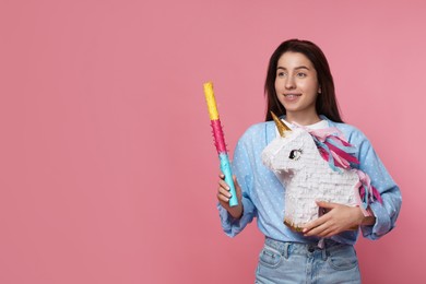 Photo of Happy woman with unicorn shaped pinata and stick on pink background, space for text