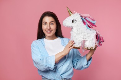 Photo of Happy woman with unicorn shaped pinata on pink background