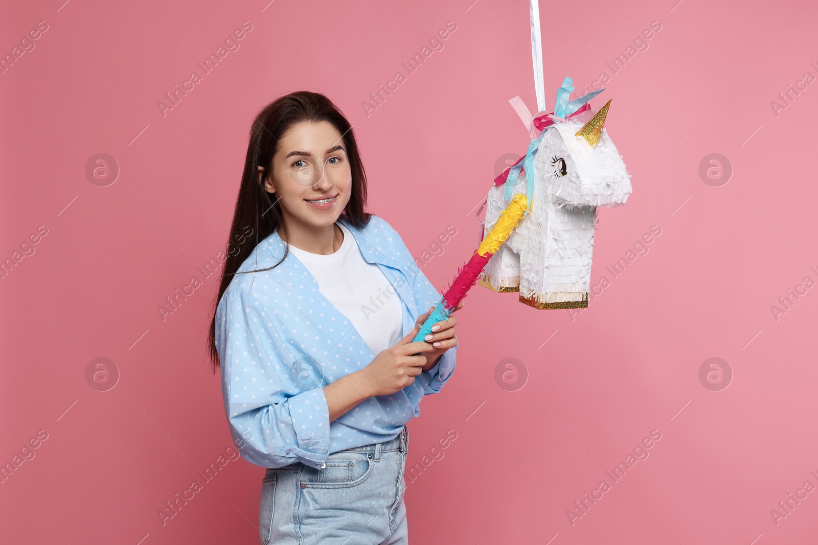 Photo of Happy woman with unicorn shaped pinata and stick on pink background