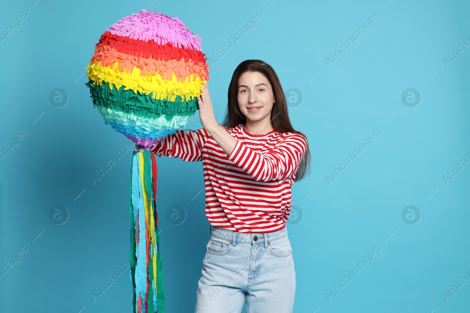 Photo of Happy woman with pinata on light blue background