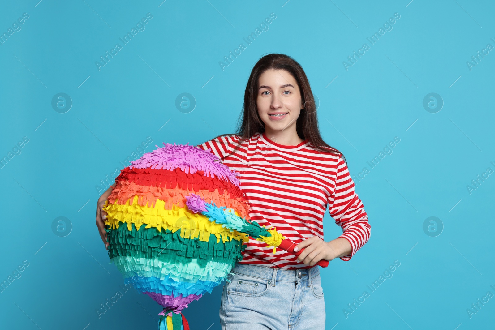 Photo of Happy woman with colorful pinata and stick on light blue background