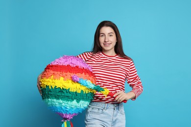 Photo of Happy woman with colorful pinata and stick on light blue background