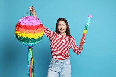 Photo of Happy woman with colorful pinata and stick on light blue background