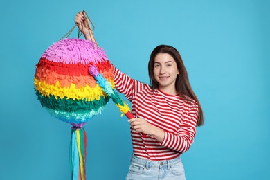 Photo of Happy woman with colorful pinata and stick on light blue background