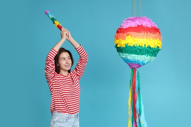 Photo of Happy woman hitting colorful pinata with stick on light blue background