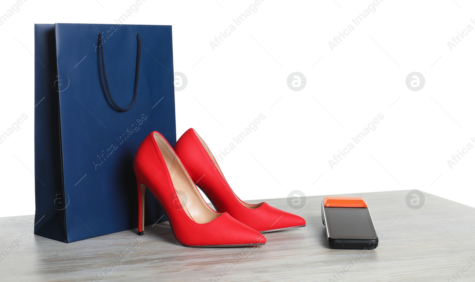 Photo of Payment terminal, shopping bag and high heeled shoes on wooden table against white background