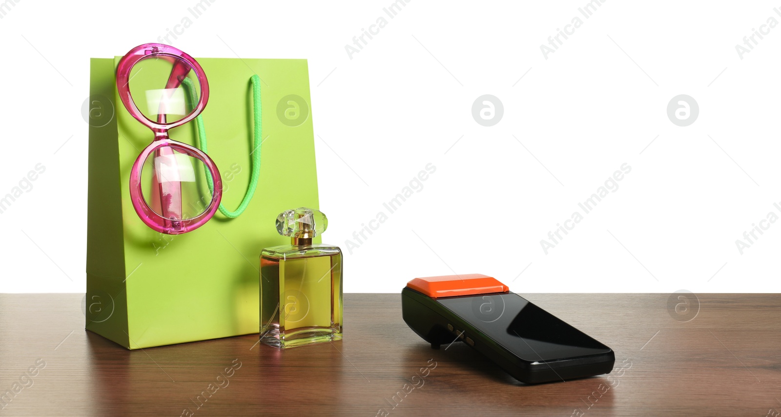 Photo of Payment terminal, perfume, sunglasses and shopping bag on wooden table against white background