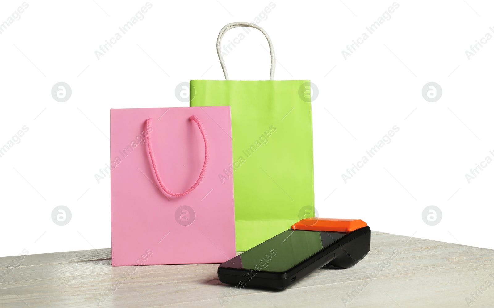 Photo of Payment terminal and shopping bags on wooden table against white background