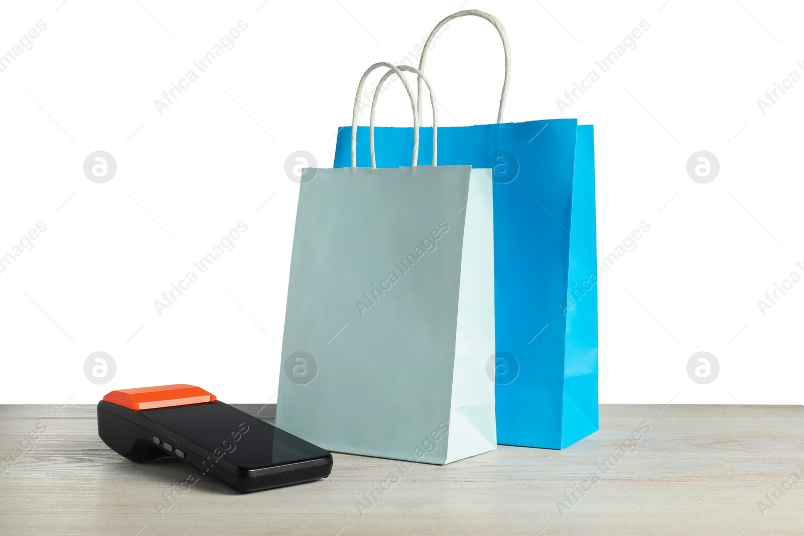 Photo of Payment terminal and shopping bags on wooden table against white background