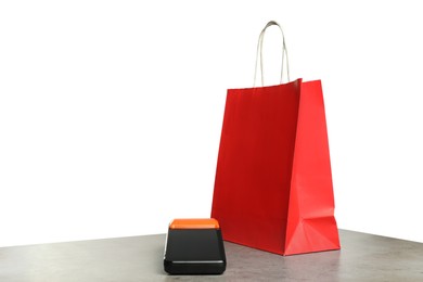 Photo of Payment terminal and shopping bag on grey table against white background