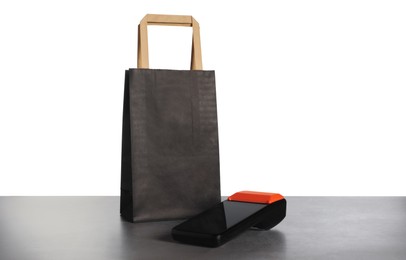 Photo of Payment terminal and shopping bag on grey table against white background