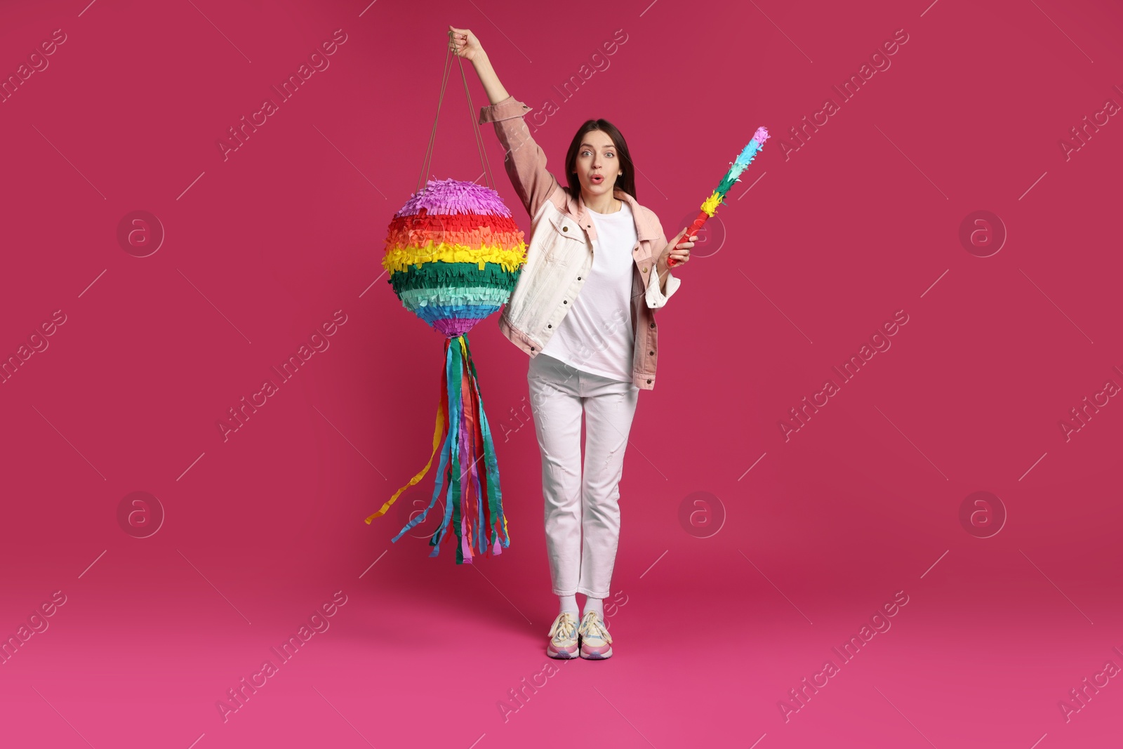 Photo of Emotional woman with colorful pinata and stick on pink background