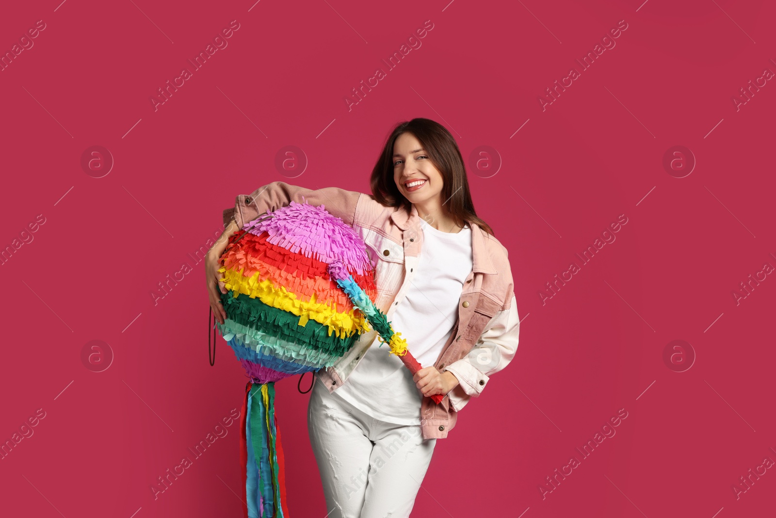 Photo of Happy woman with colorful pinata and stick on pink background