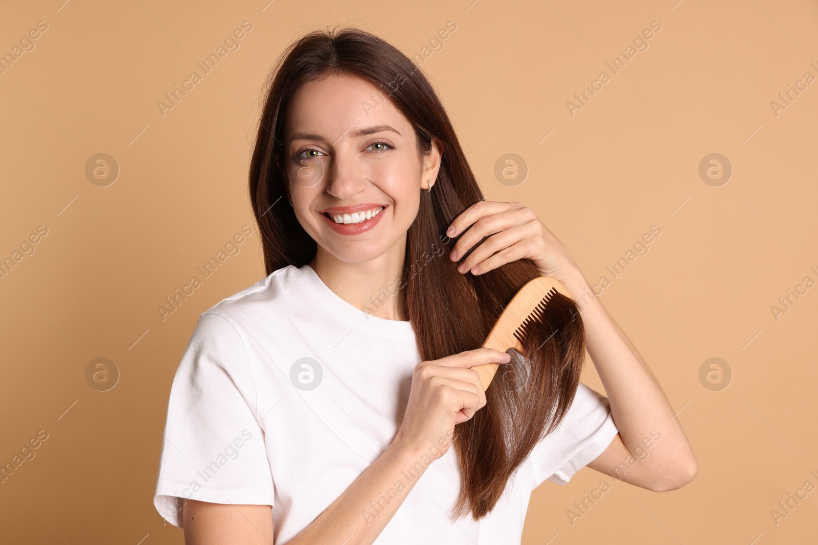 Photo of Smiling woman brushing her hair with comb on beige background