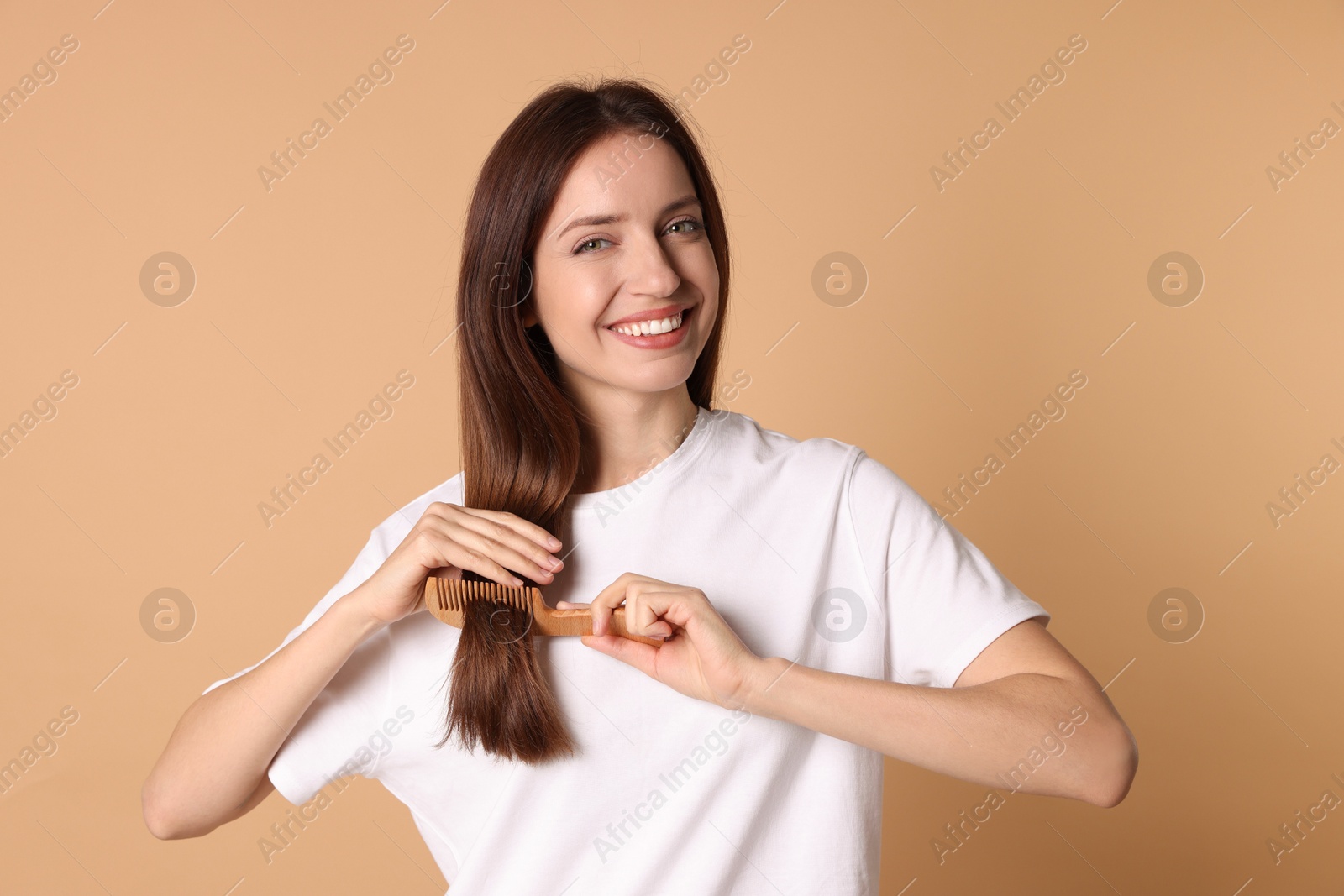 Photo of Smiling woman brushing her hair with comb on beige background