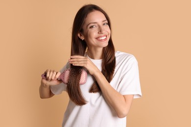 Photo of Smiling woman brushing her hair on beige background