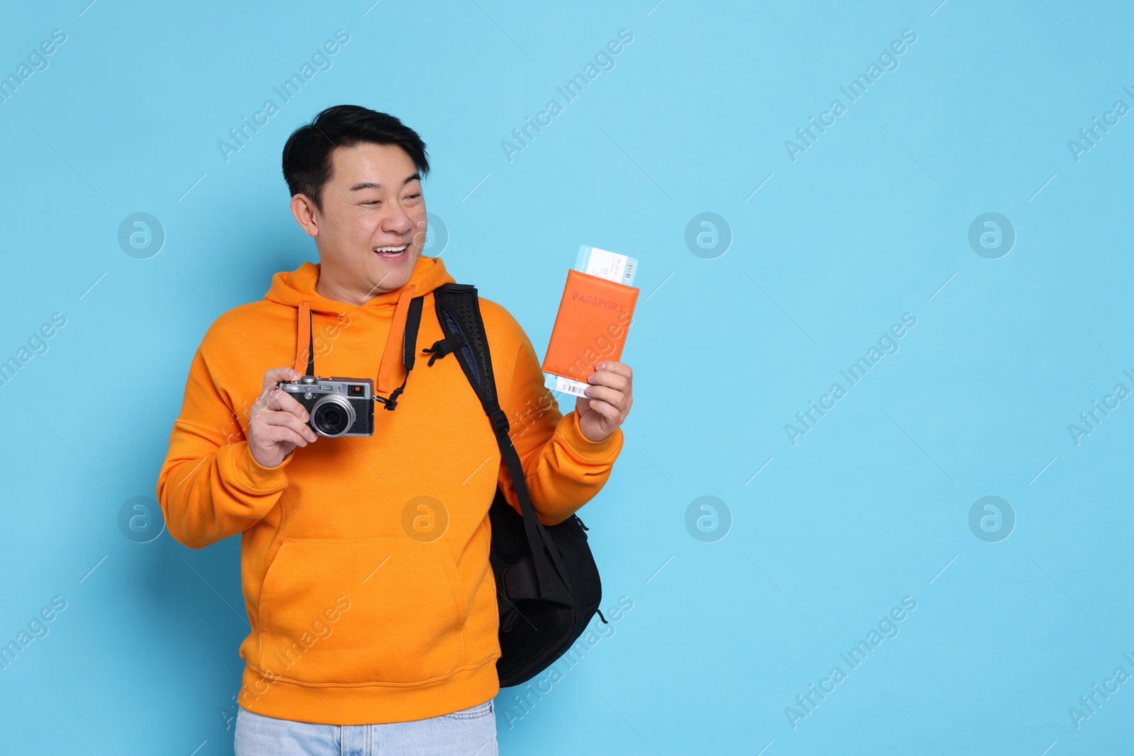 Photo of Happy traveller with passport and camera on light blue background. Space for text