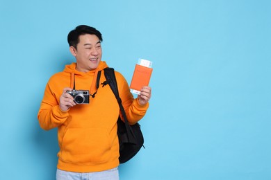 Photo of Happy traveller with passport and camera on light blue background. Space for text