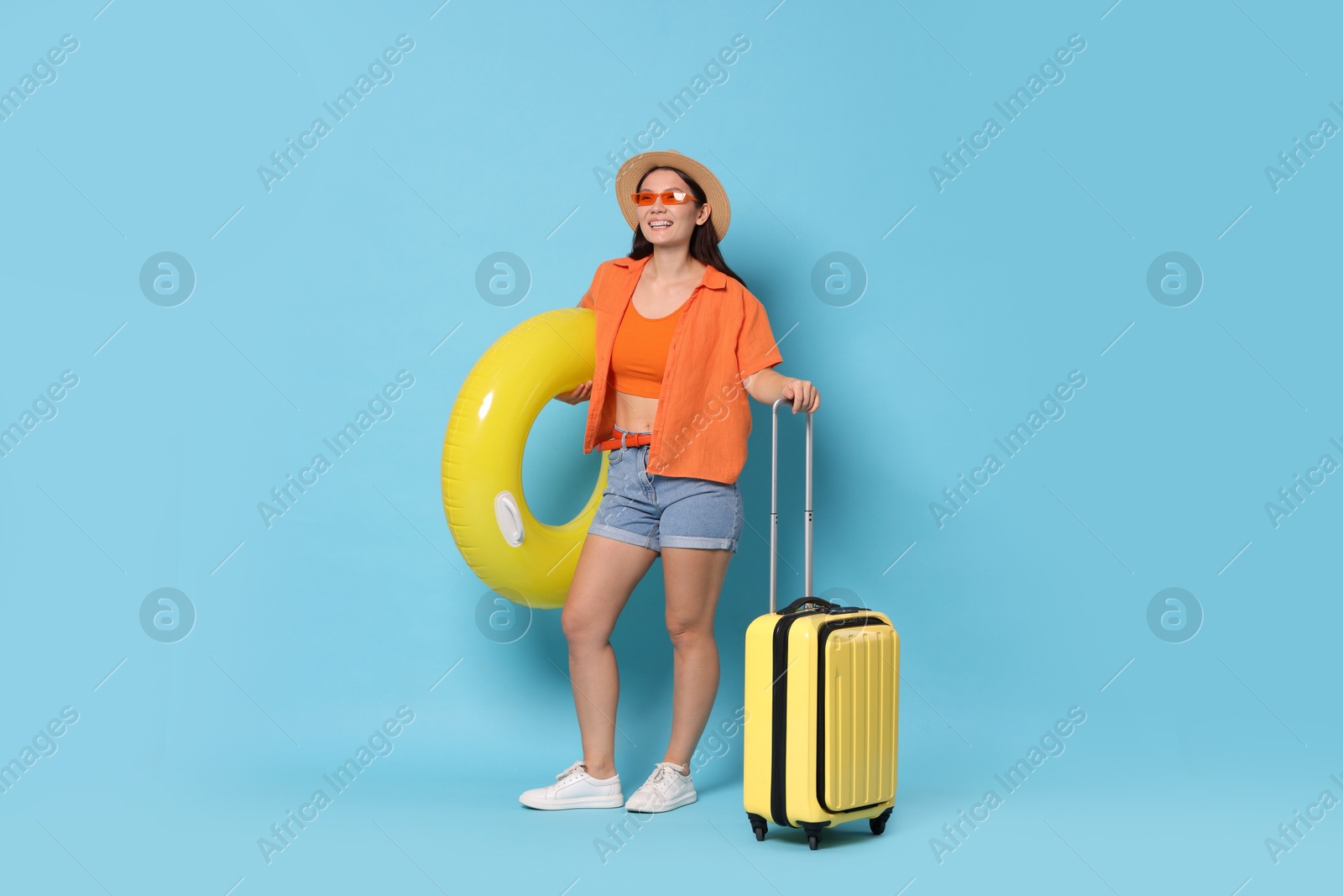 Photo of Happy traveller with inflatable ring and suitcase on light blue background