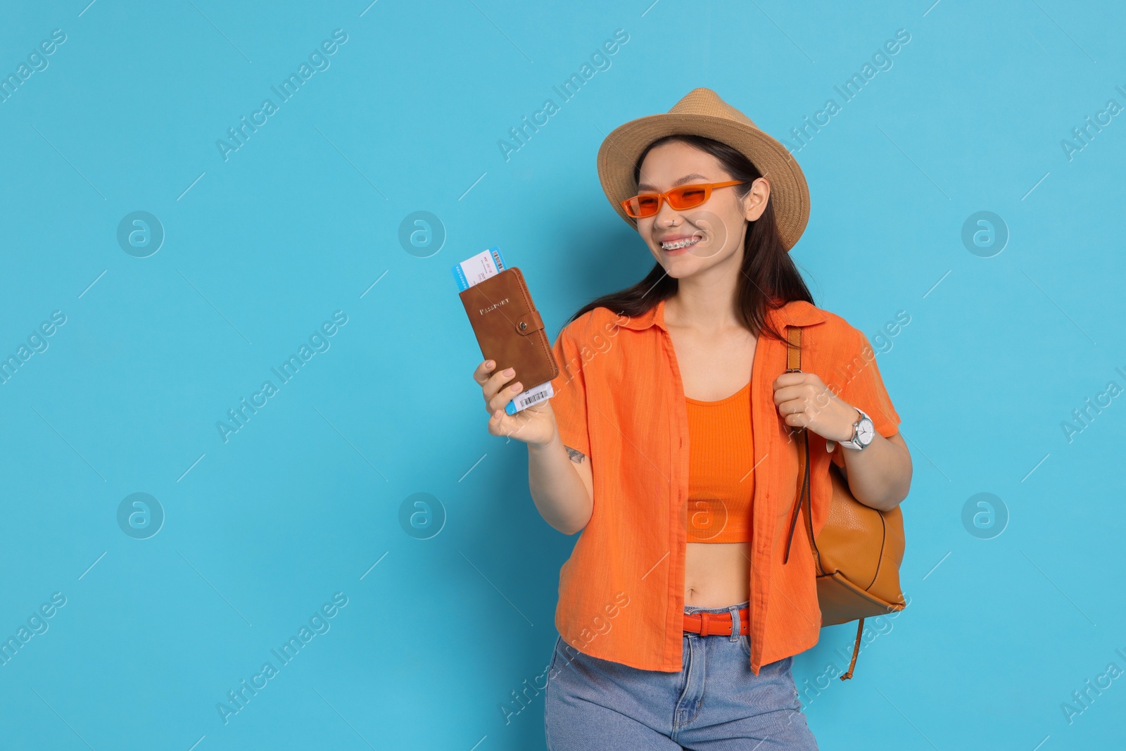 Photo of Happy traveller with backpack and passport on light blue background. Space for text