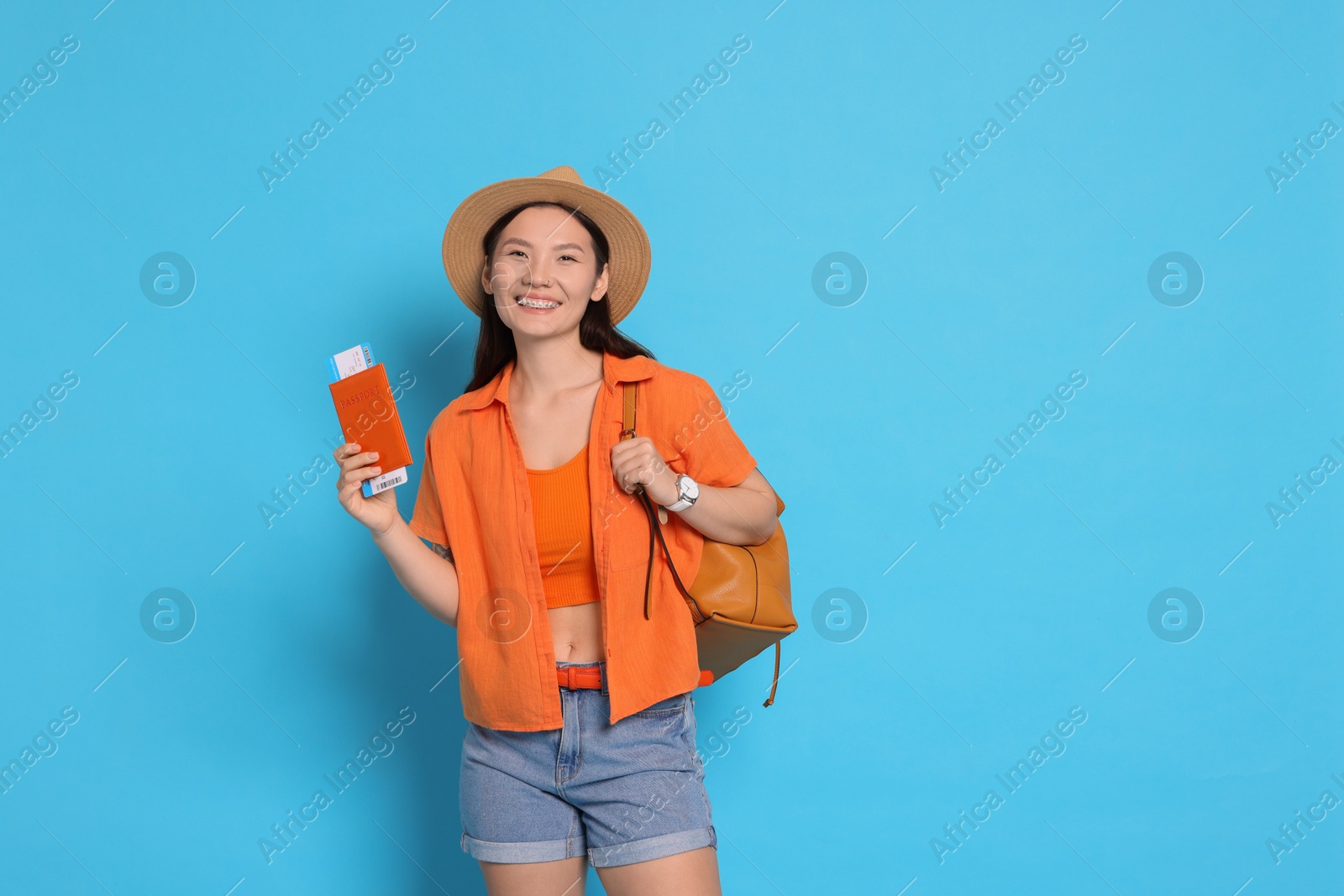 Photo of Happy traveller with backpack and passport on light blue background. Space for text