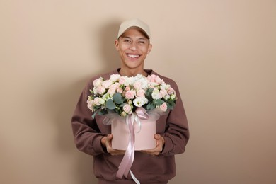 Photo of Smiling delivery man holding gift box with beautiful floral composition on beige background