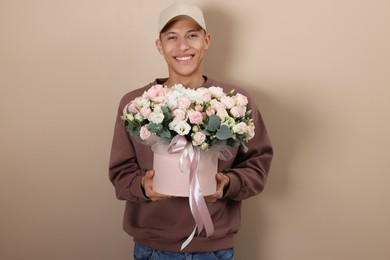 Photo of Smiling delivery man holding gift box with beautiful floral composition on beige background