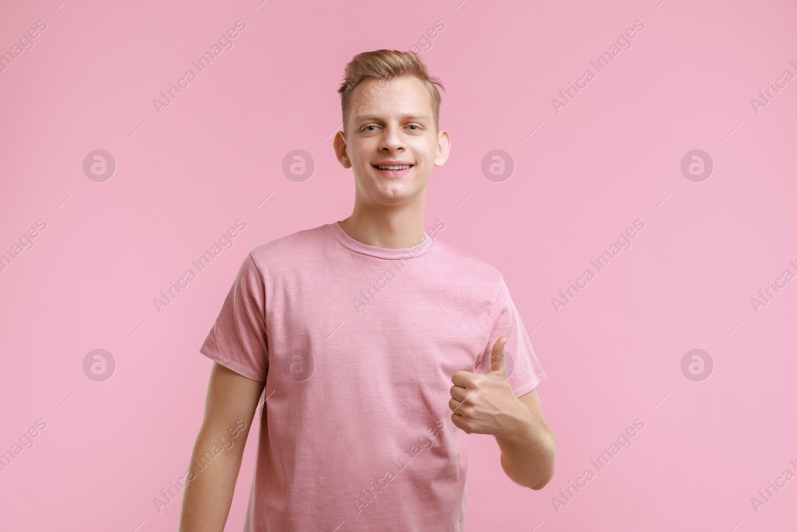 Photo of Happy man showing thumbs up on pink background. Like gesture