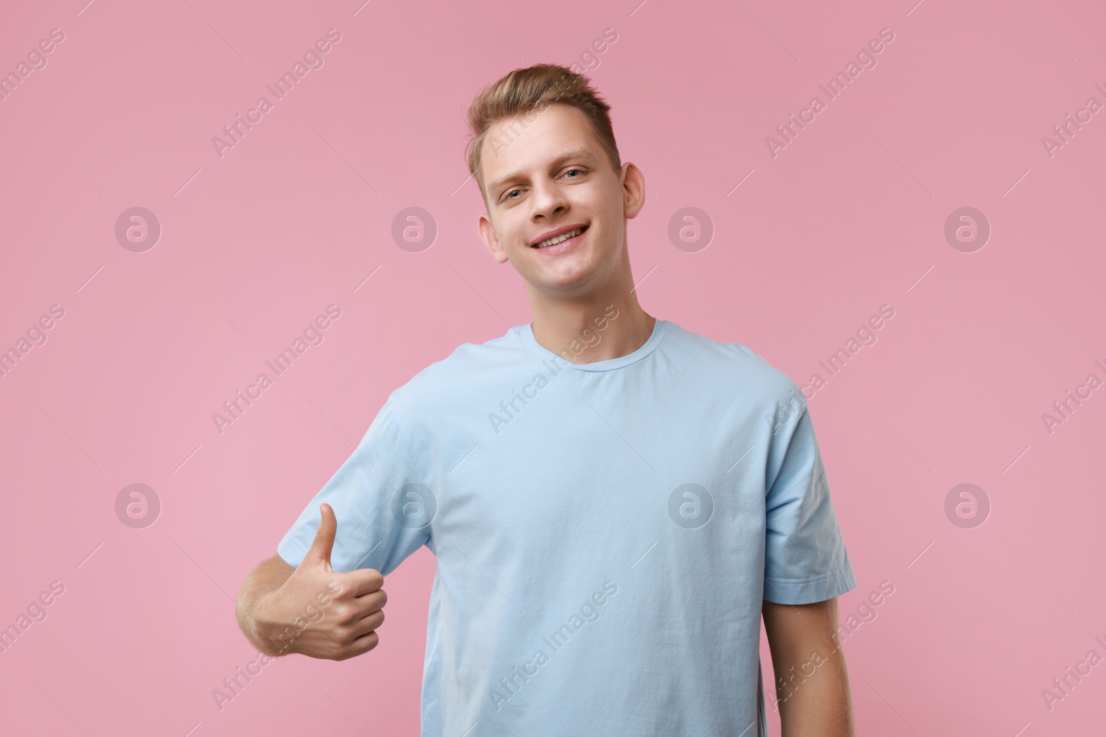 Photo of Happy man showing thumbs up on pink background. Like gesture