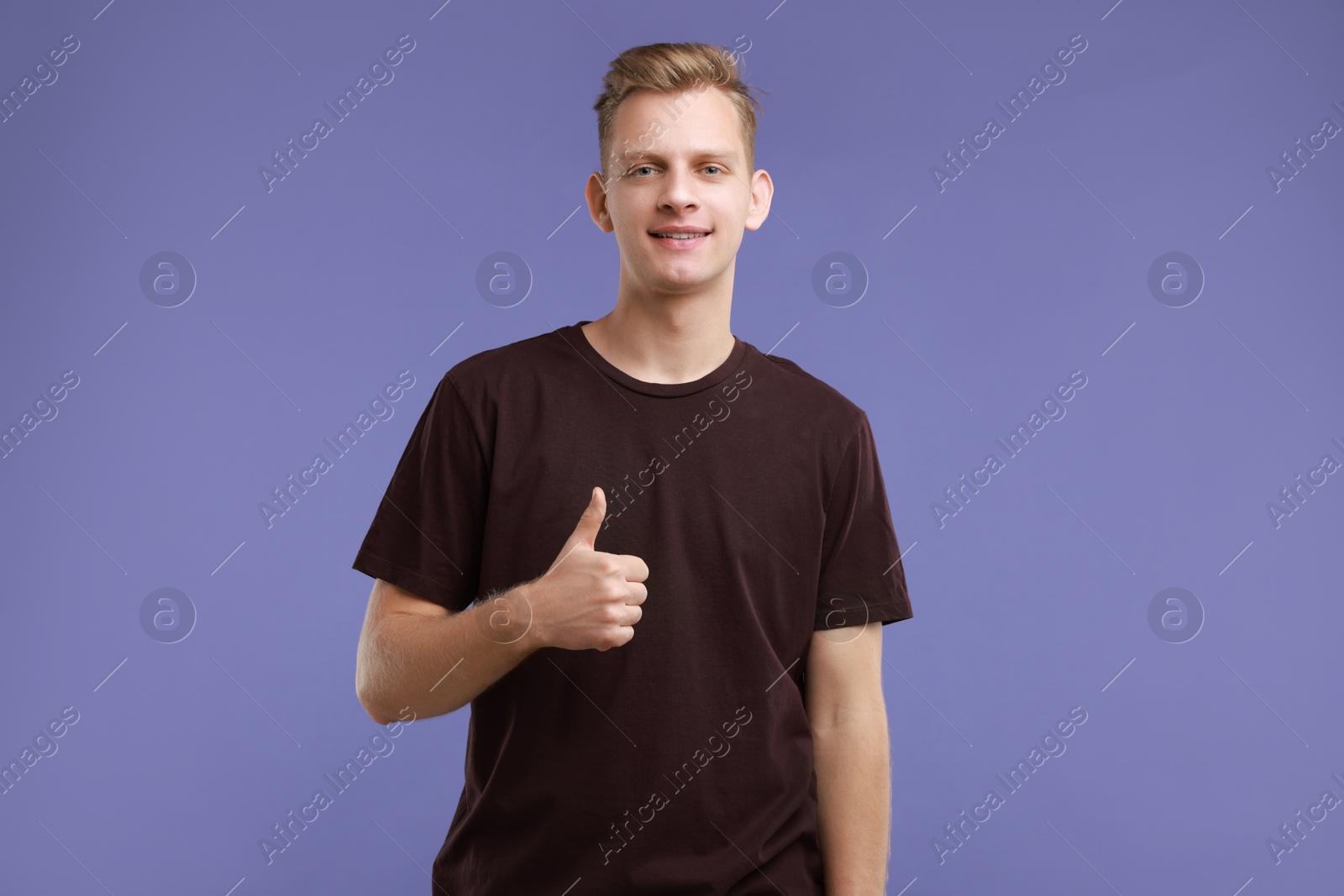 Photo of Happy man showing thumbs up on purple background. Like gesture