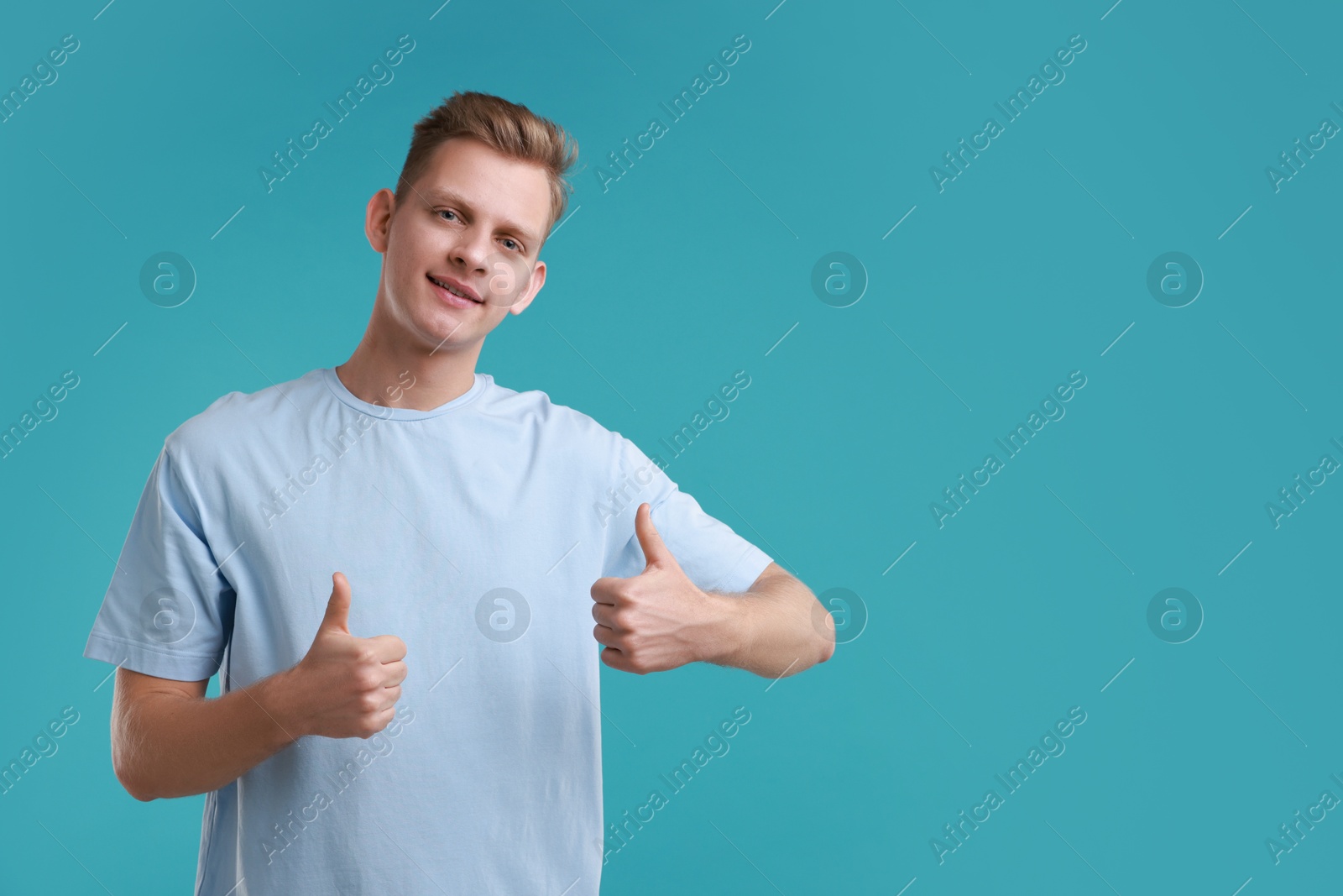 Photo of Happy man showing thumbs up on light blue background, space for text. Like gesture