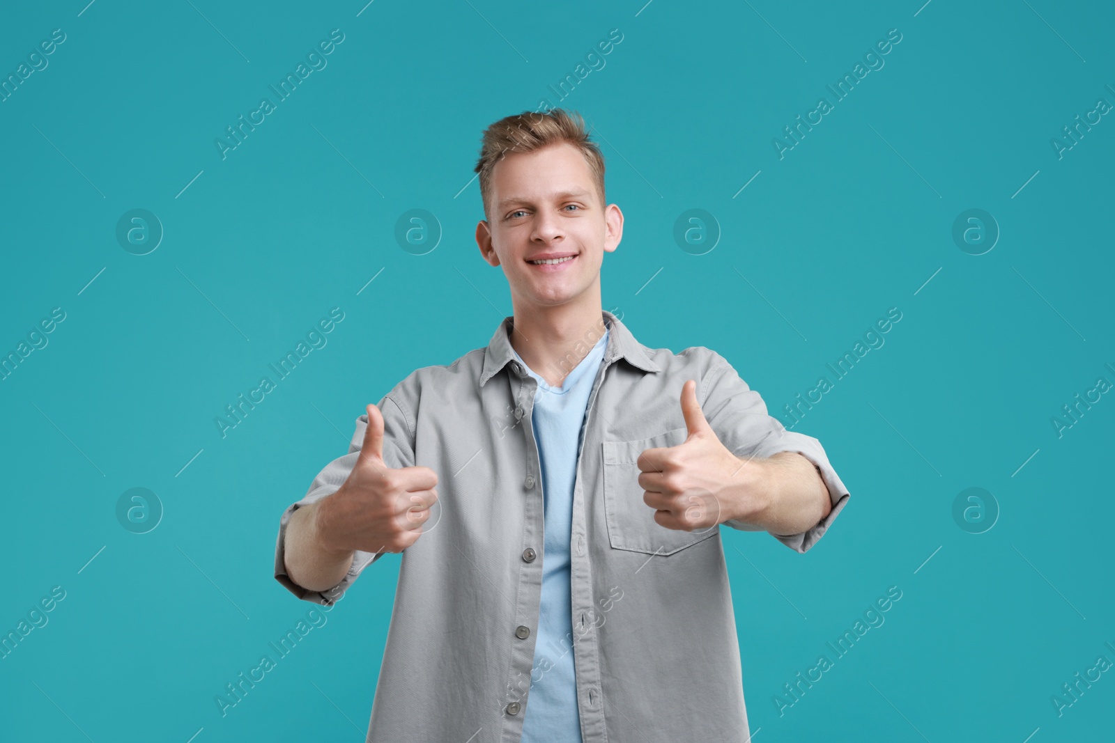 Photo of Happy man showing thumbs up on light blue background. Like gesture