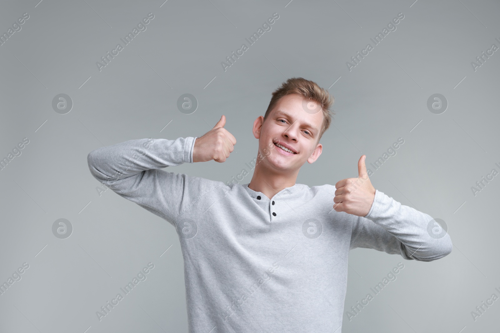 Photo of Happy man showing thumbs up on grey background. Like gesture