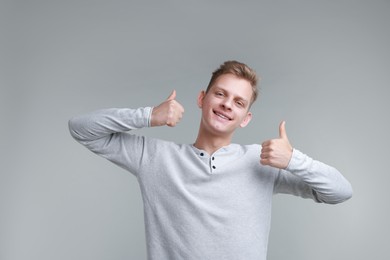 Happy man showing thumbs up on grey background. Like gesture