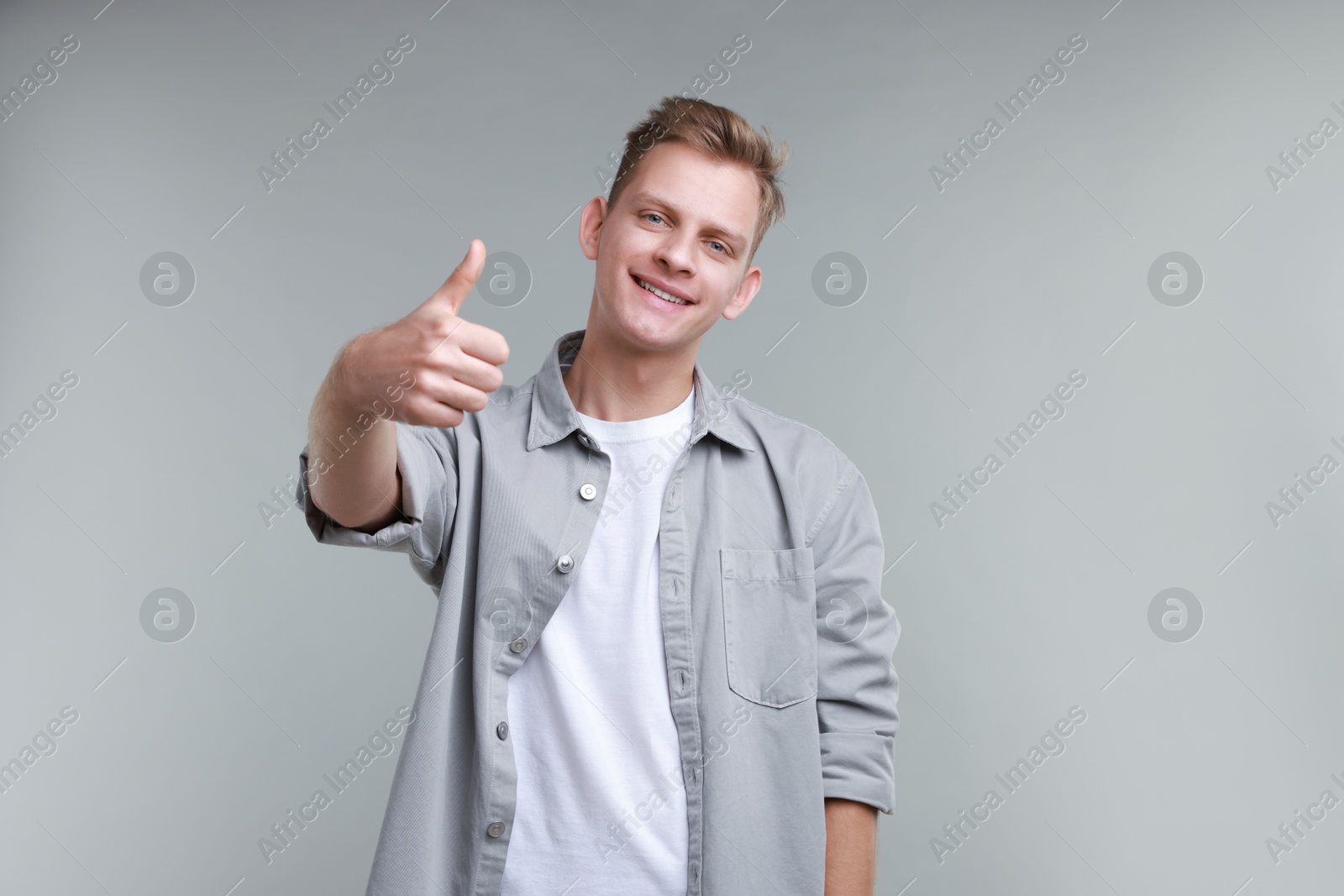 Photo of Happy man showing thumbs up on grey background. Like gesture