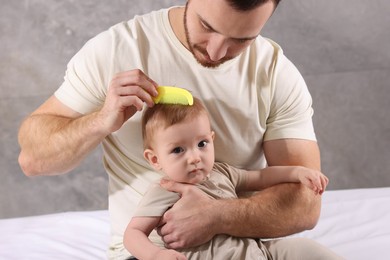 Photo of Man brushing hair of his little baby on bed indoors