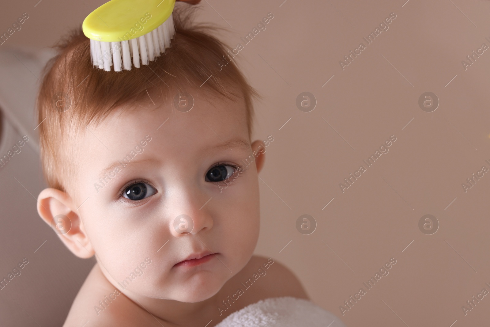 Photo of Mother brushing hair of her little baby on dark beige background, closeup. Space for text