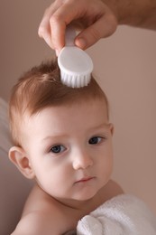 Photo of Parents brushing hair of their little baby on dark beige background, closeup