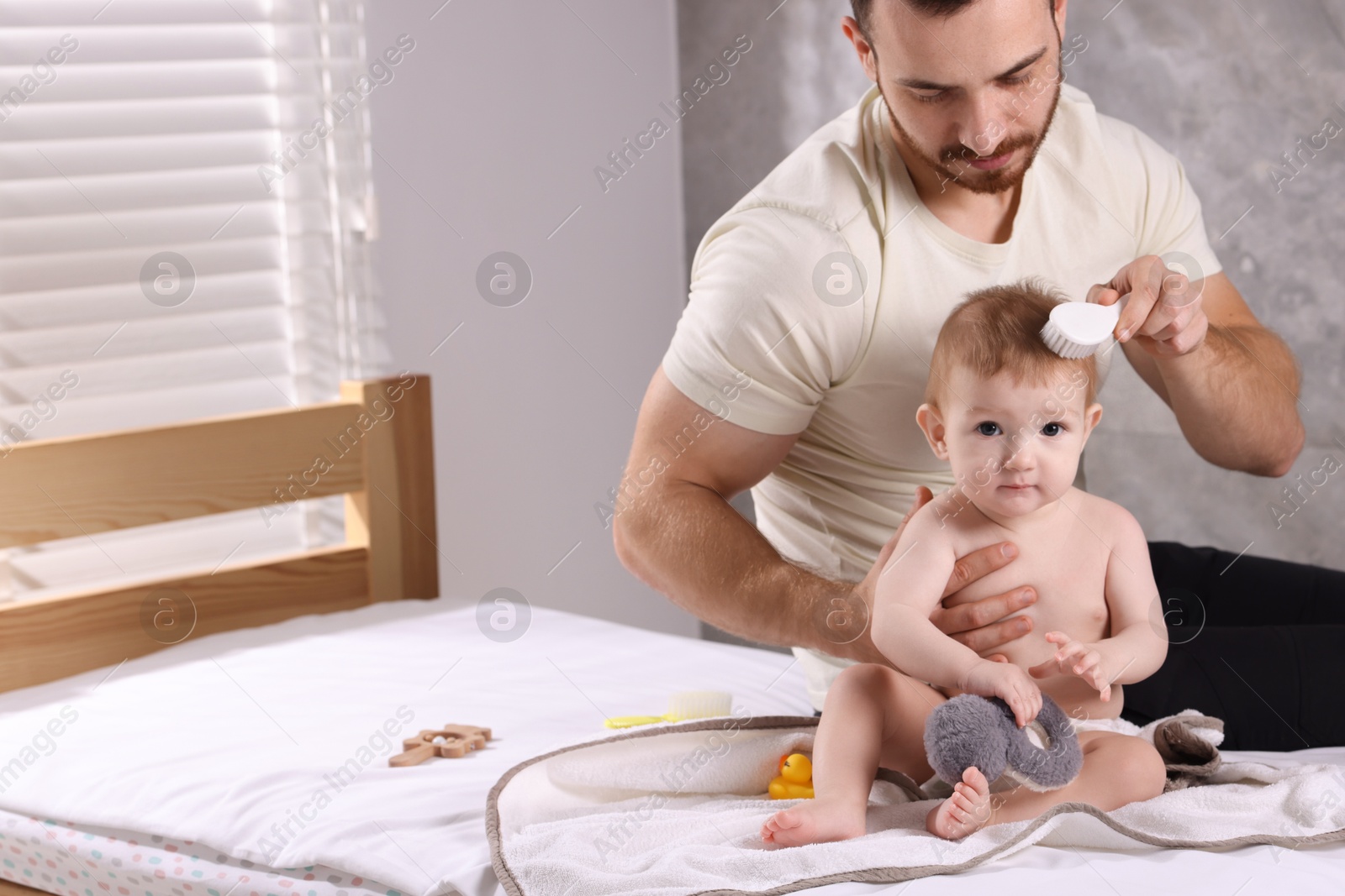 Photo of Man brushing hair of his little baby on bed indoors, space for text