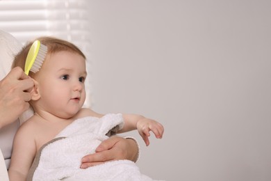 Photo of Woman brushing hair of her little baby indoors, closeup. Space for text