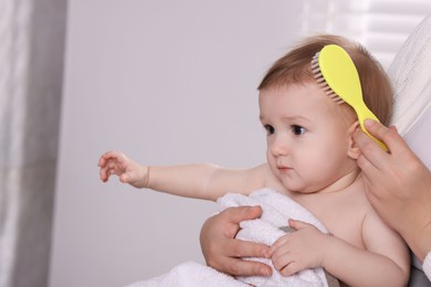 Photo of Woman brushing hair of her little baby indoors, closeup. Space for text