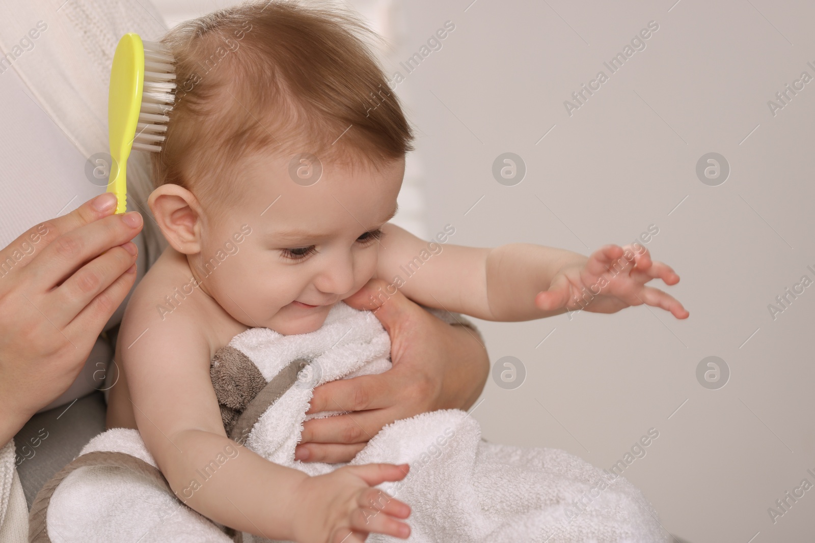 Photo of Woman brushing hair of her little baby indoors, closeup