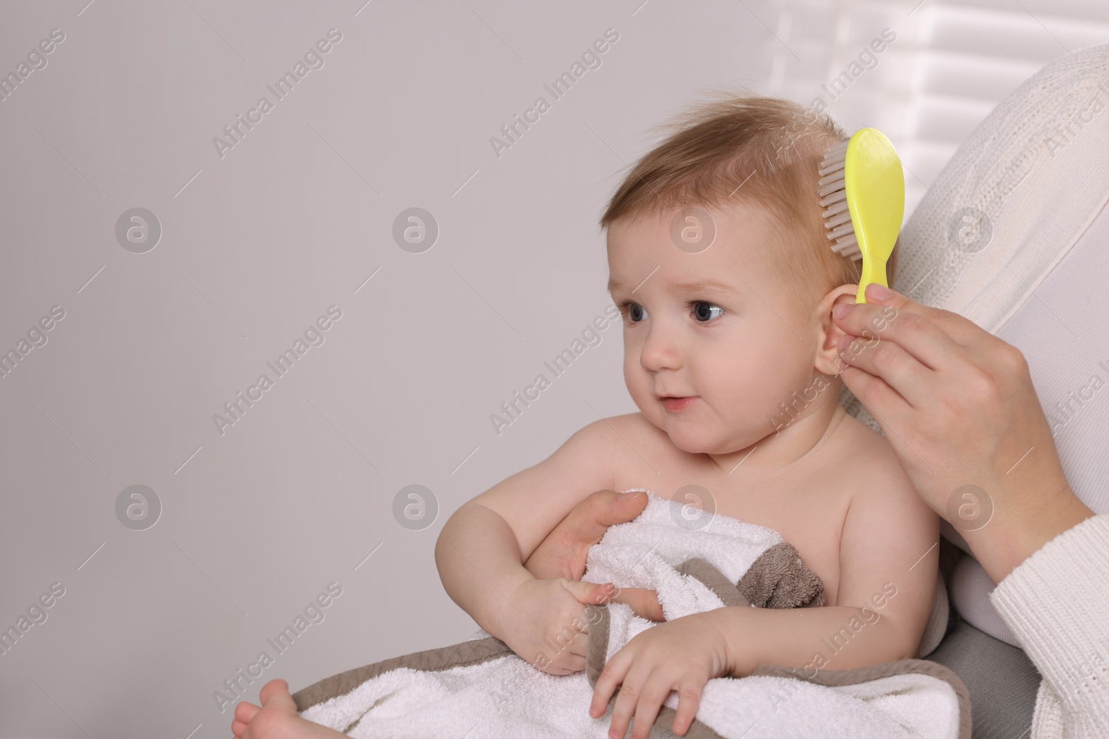 Photo of Woman brushing hair of her little baby indoors, closeup. Space for text