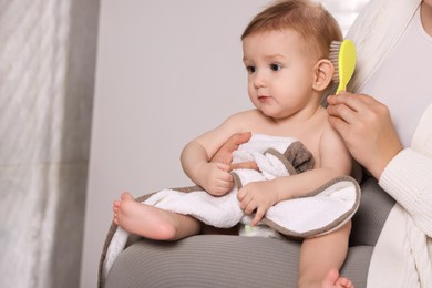 Photo of Woman brushing hair of her little baby indoors, closeup. Space for text