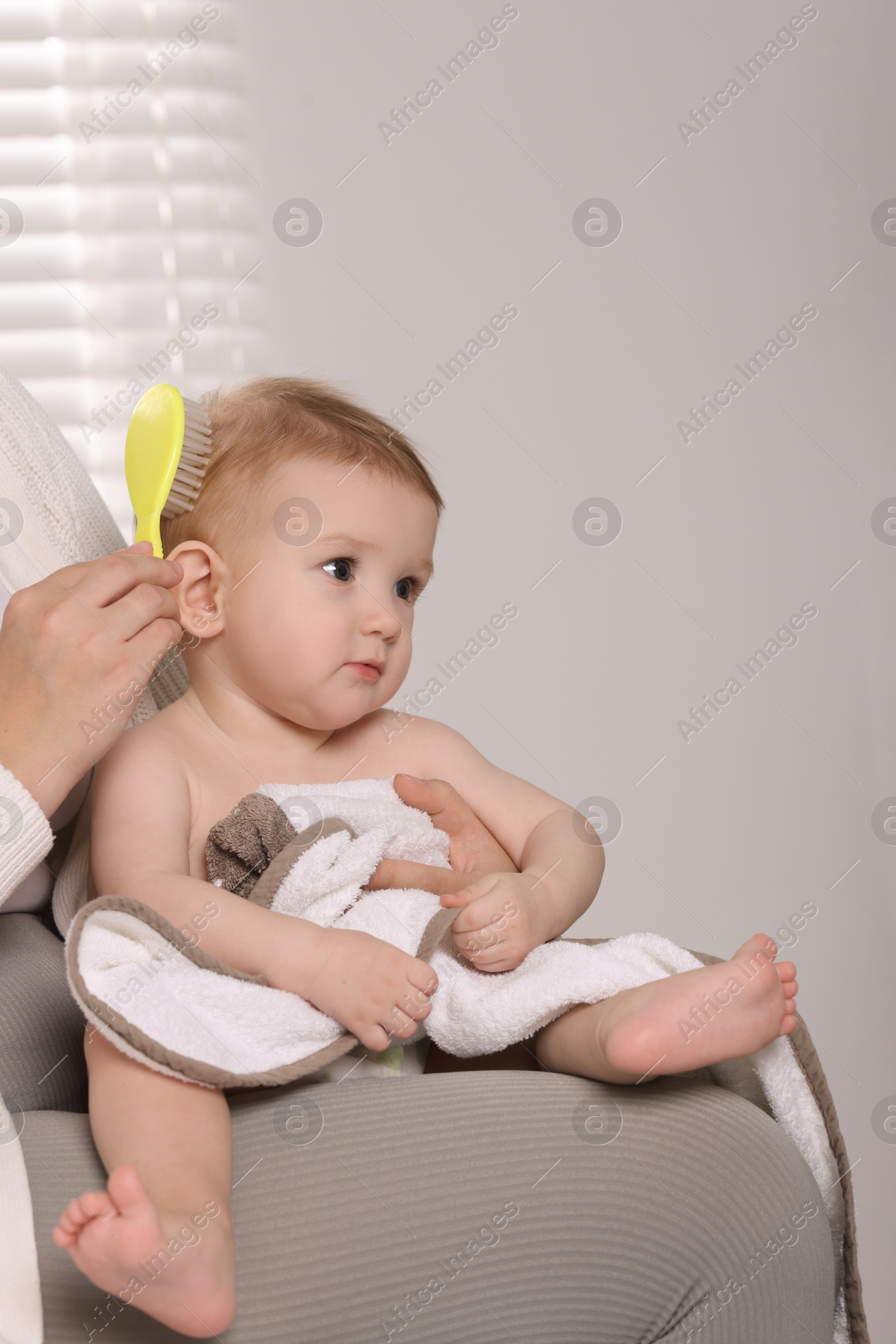 Photo of Woman brushing hair of her little baby indoors, closeup