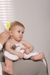 Photo of Woman brushing hair of her little baby indoors, closeup