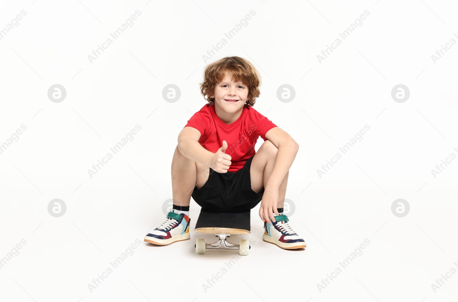 Photo of Little boy with skateboard showing thumbs up on white background