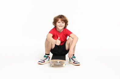 Photo of Little boy with skateboard showing thumbs up on white background