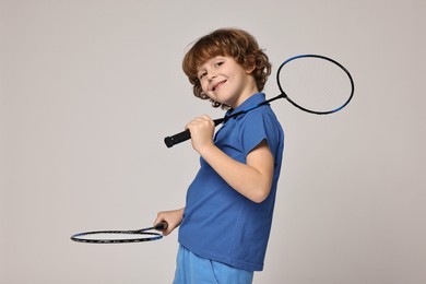 Little boy with badminton rackets on light grey background