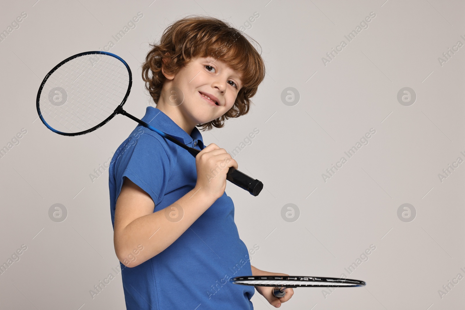 Photo of Little boy with badminton rackets on light grey background, space for text